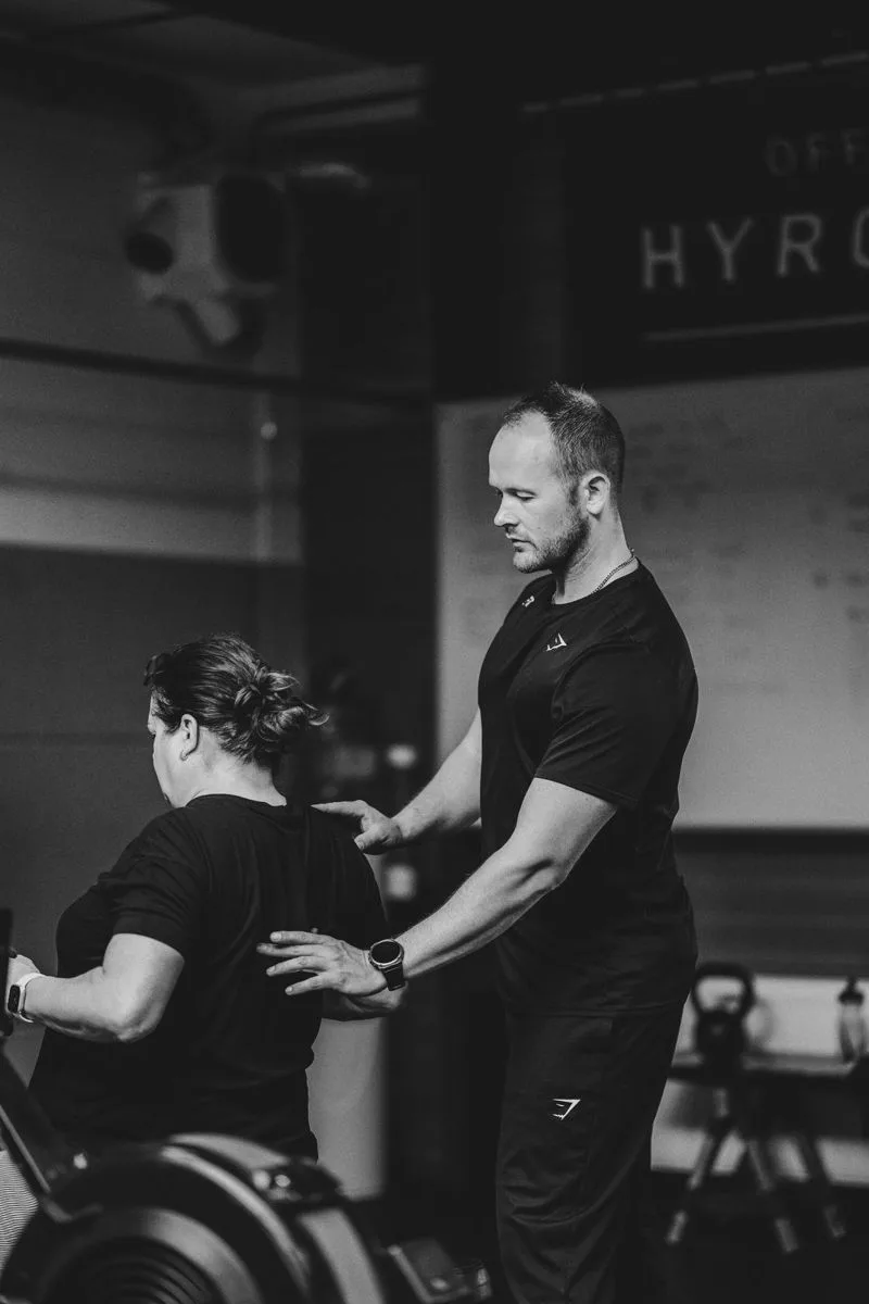 Een personal trainer corrigeert de houding van een klant op de roeimachine